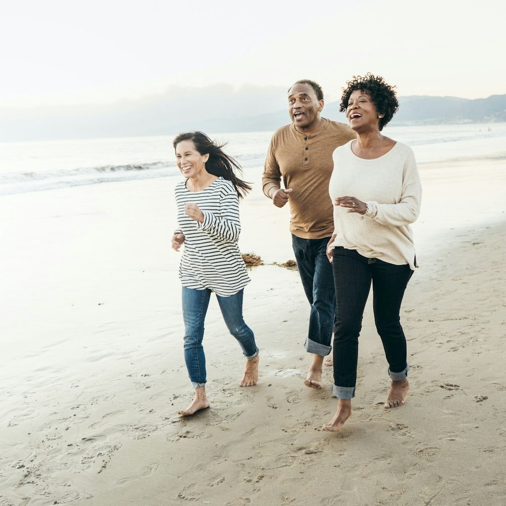 Two woman and a man running on the beach and laughing